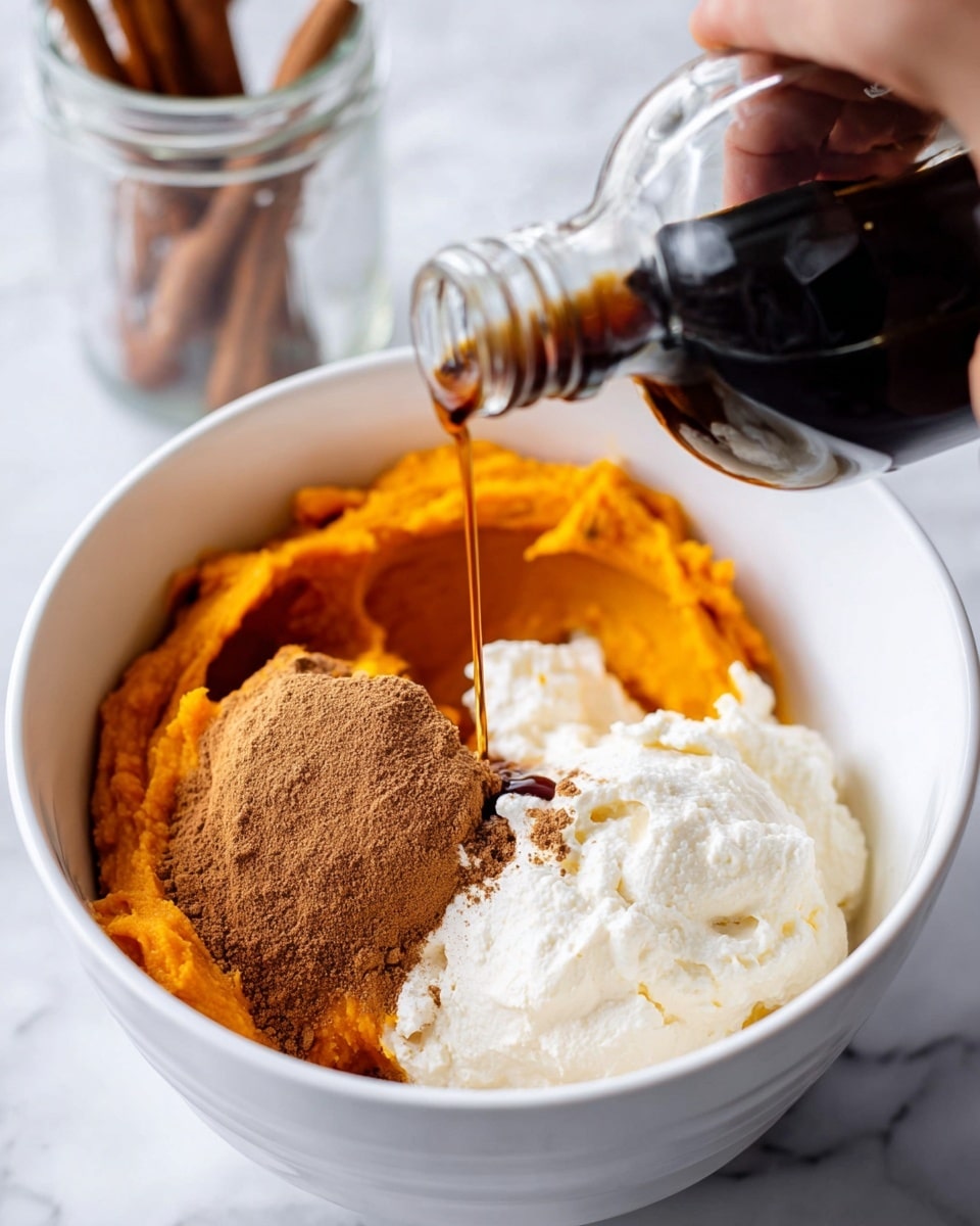 The dish is served in a white bowl placed on a white marbled textured surface and shows two main layers. The bottom layer is a smooth, thick, creamy orange mixture that fills the bowl. On top, there is a swirl of the same orange cream in the center, dusted lightly with a brown powder, likely cinnamon. To one side of the swirl, there is a row of light brown granola or oats arranged neatly, adding texture and contrast. A shiny drizzle of amber syrup covers part of the swirl, creating a glossy effect. A gold spoon lies nearby on the white marbled surface. Photo taken with an iphone --ar 4:5 --v 7