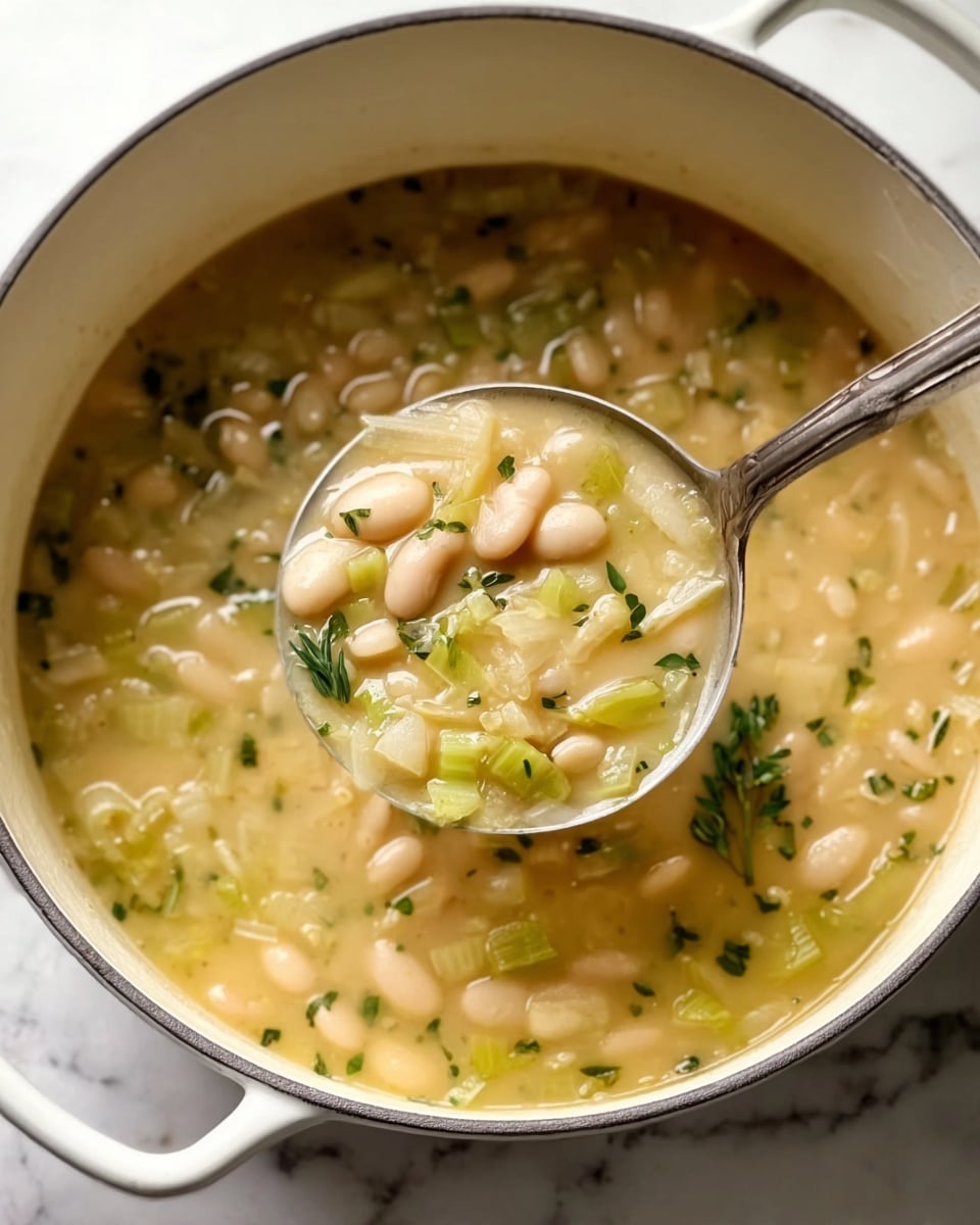 A top view of a white large pot filled with creamy white bean stew mixed with small chopped green vegetables, likely celery or leeks, visible in a thick light greenish-yellow sauce. The stew is garnished with small sprigs of thyme and black pepper sprinkled on top. The pot is placed on a white marbled surface with a white cloth nearby, a small bowl of finely chopped green herbs in the upper left corner, and fresh sprigs of thyme on the upper right side. A wooden-handled spatula with a black head is partially visible in the bottom right corner. photo taken with an iphone --ar 4:5 --v 7