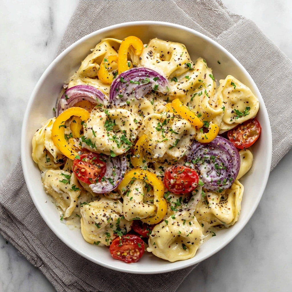 A white bowl filled with creamy tortellini pasta that is light yellow in color and coated in a thick white sauce. Scattered throughout the dish are red cherry tomato halves, thin purple onion slices, and small pieces of crispy brown bacon. There are also yellow pepper rings adding a pop of color. The pasta and toppings are sprinkled with green herbs and crushed black pepper. The bowl sits on a light gray cloth over a white marbled surface. Photo taken with an iphone --ar 4:5 --v 7