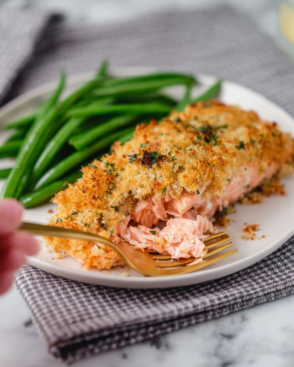 A large piece of cooked salmon fillet lies on crinkled silver foil covering a white marbled surface. The top layer of salmon is covered with a thick, golden-brown breadcrumb crust mixed with small green herb pieces and some sesame seeds, creating a rough texture. The pinkish-orange salmon underneath shows through slightly along the edges. Around the salmon, there are several bright yellow lemon slices laid out evenly, topped with small green herb bits. The whole scene is bright and clean with natural lighting, capturing the textures and colors clearly. photo taken with an iphone --ar 4:5 --v 7