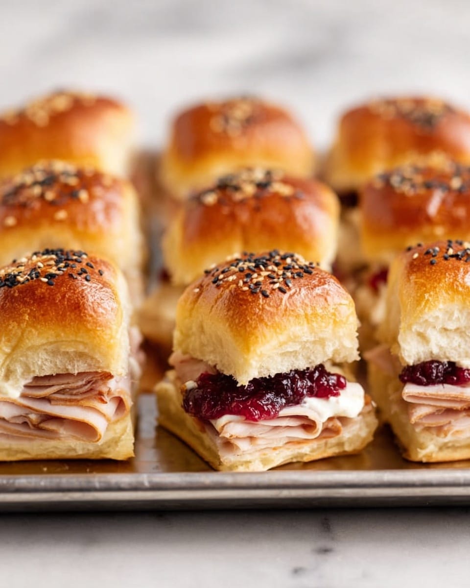 The image shows a baking tray filled with small square sandwiches made of shiny, golden brown buns topped with white and black sesame seeds. Each sandwich has soft, fluffy layers: the top layer is the bun with a smooth, slightly shiny texture, the middle layer shows sliced turkey meat in light pinkish-white, and a bright red layer of cranberry sauce underneath. One sandwich is pulled slightly away from the tray, revealing the layers inside clearly. The tray is placed on a white marbled surface. photo taken with an iphone --ar 4:5 --v 7