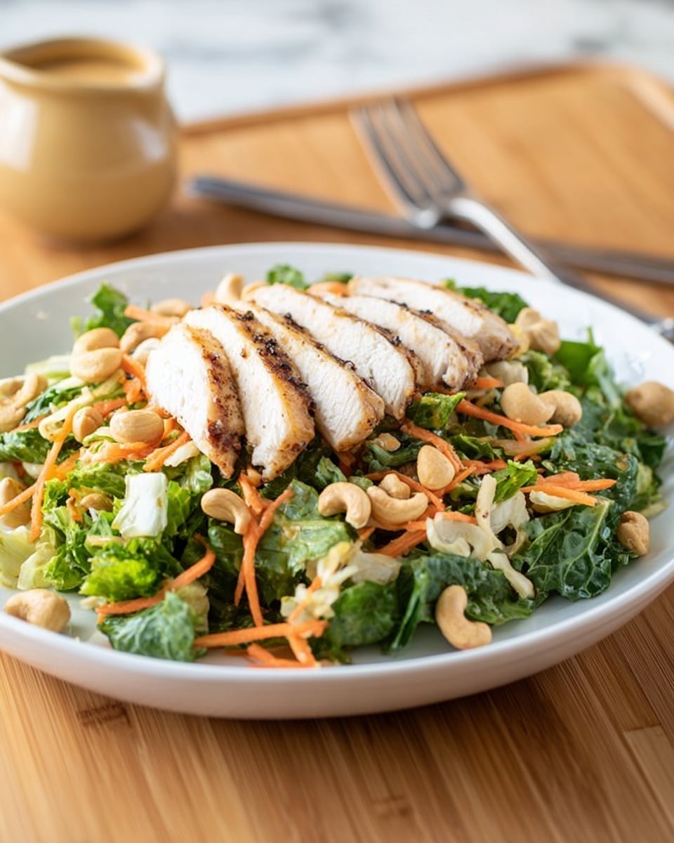 A white plate holds a fresh salad layered with chopped green leafy vegetables and shredded orange carrots as the base. Scattered on top are whole cashew nuts, adding a light beige color and smooth texture. On the upper part of the salad are five slices of grilled chicken breast, showing a white inside with a lightly browned and seasoned outside. The plate is on a wooden surface with a fork to the right and a small light brown container in the background, all set against a white marbled texture. photo taken with an iphone --ar 4:5 --v 7