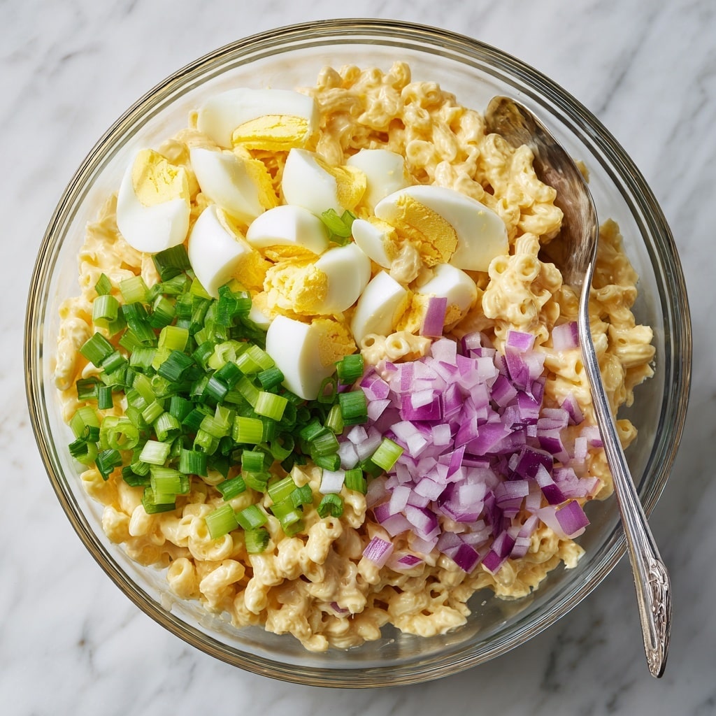 A close-up view of a white bowl filled with creamy macaroni salad, showing a thick layer of small elbow macaroni coated in a pale yellow mayonnaise mixture. Mixed in are small pieces of red bacon bits and finely chopped green onions scattered on top, adding pops of red and green color. The macaroni is generously sprinkled with a reddish-orange paprika dusting. Inside the bowl, the texture looks smooth and creamy with small chunks of onion visible within the salad. The bowl sits on a wooden surface with part of a black plate and two silver forks visible at the bottom left corner. photo taken with an iphone --ar 4:5 --v 7