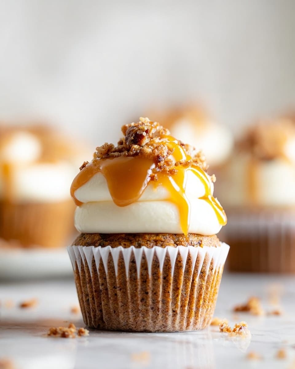 A close-up of a cupcake with three main layers: the bottom light brown cake layer with a soft, crumbly texture, topped with a thick swirl of creamy white frosting, and finished with a drizzle of shiny caramel sauce and crunchy chopped nuts scattered on top. The cupcake liner is peeled back slightly, showing the cake inside, and a silver fork holds a bite-sized piece of the cake covered in frosting and caramel, resting on a white marbled surface. In the background, more cupcakes on a white plate are softly blurred. Photo taken with an iphone --ar 4:5 --v 7