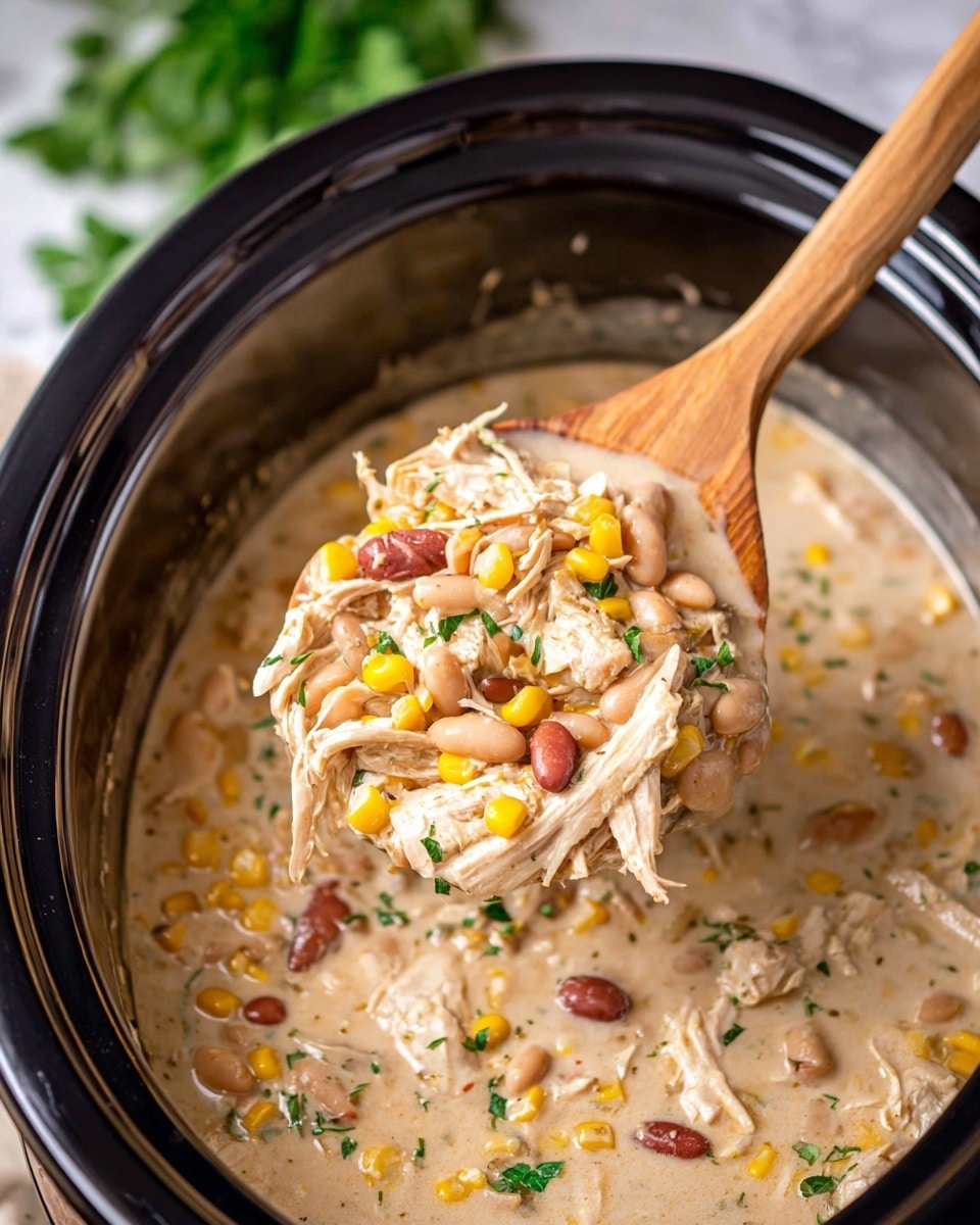 A black slow cooker filled with a creamy, light beige chicken stew containing visible shredded chicken pieces, white beans, red beans, yellow corn kernels, and small green herb sprinkles spread throughout. A wooden spoon lifts a portion of the stew, showing the mix of stringy chicken, smooth beans, and corn in a rich, thick broth with a few translucent onion pieces. The background is a white marbled texture with blurred green herbs. photo taken with an iphone --ar 4:5 --v 7
