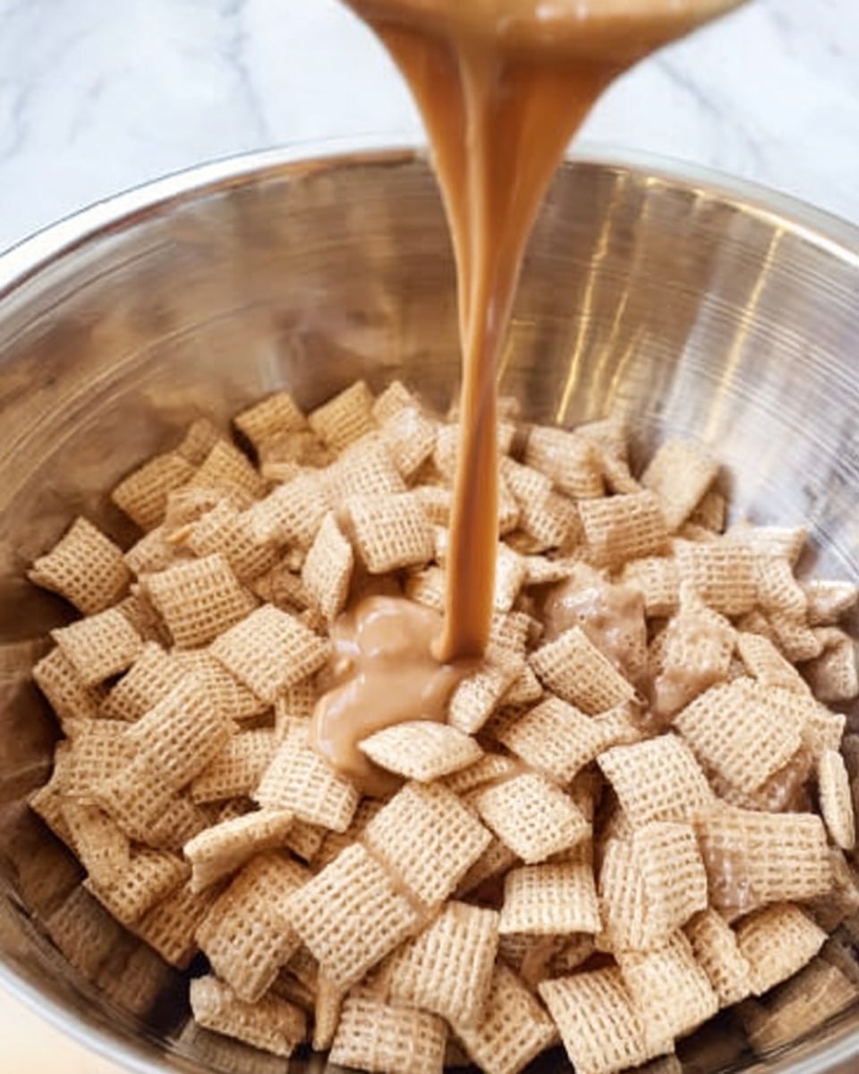 A close-up image shows a large silver mixing bowl filled with square, light beige cereal pieces with a woven texture. A smooth, caramel-colored liquid is being poured from above into the bowl, flowing down into the cereal and creating a glossy contrast between the dry cereal and the thick liquid. The background is a white marbled texture. Photo taken with an iphone --ar 4:5 --v 7