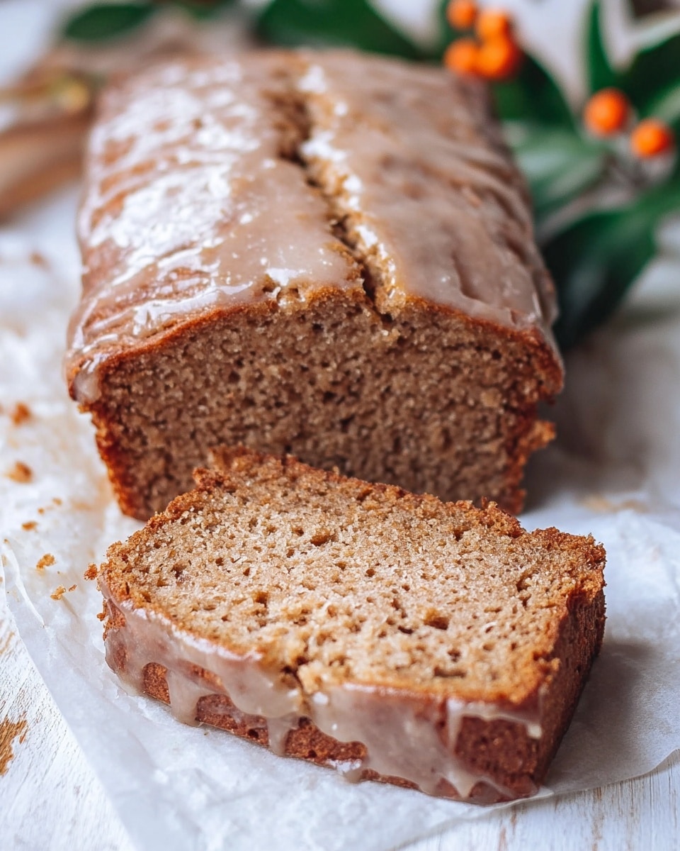 A loaf of brown quick bread with a cracked glaze on top is sliced to show its texture; the slice in front has a moist, crumbly surface with small air holes, resting on white parchment paper over a white marbled surface. The loaf in the back shows the same glaze and brown crumb with a rough edge where it was cut. Some blurred green leaves and orange berries are visible in the corners. Photo taken with an iphone --ar 4:5 --v 7