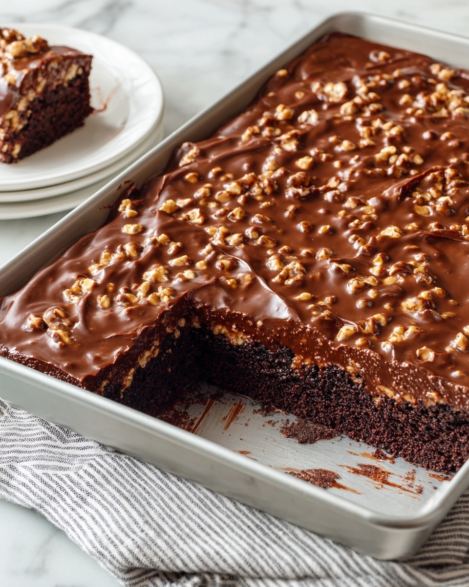 A rectangular pan holds a three-layer chocolate dessert with a bite missing from one corner. The bottom layer is dark, moist chocolate cake visible where the bite was taken. The middle layer is a thick, glossy milk chocolate frosting with small, crunchy nut pieces mixed in, spread evenly over the cake. The dessert is on a white marbled surface with a striped cloth beneath the pan. Nearby is a white plate with a small piece of the dessert, showing the same chocolate and nut topping. Photo taken with an iphone --ar 4:5 --v 7