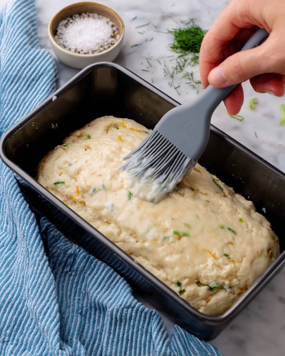 A loaf of bread is placed on a wooden board over a white marbled texture. The bread has a light golden crust with visible small pieces of herbs and onions baked inside. The loaf is partially sliced into four pieces, showing a soft, slightly crumbly, and pale interior with scattered bits of cooked onion and herbs. Next to the bread, there are sprigs of fresh rosemary and a green leafy herb, adding a natural touch to the scene. Photo taken with an iphone --ar 4:5 --v 7