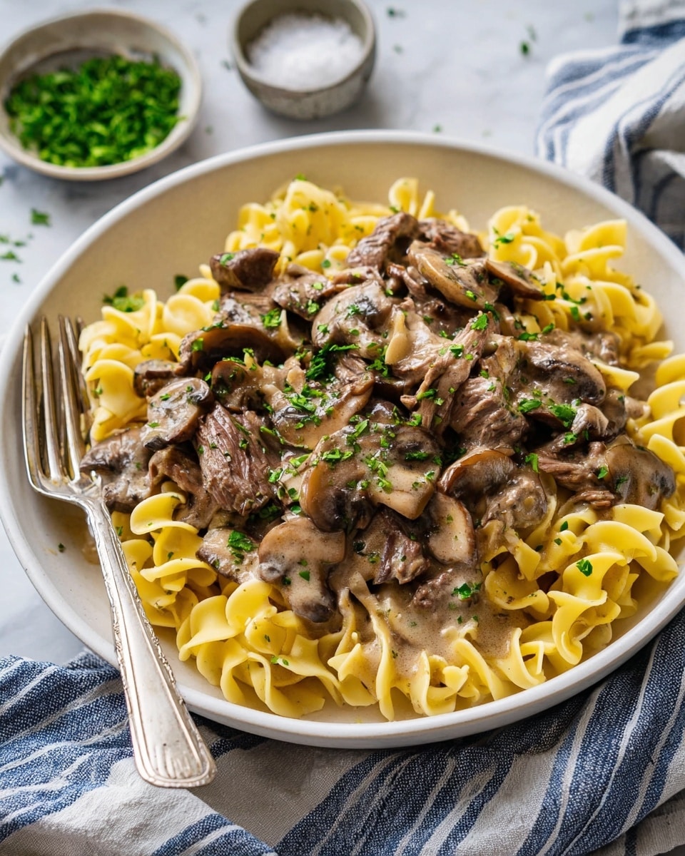 A close-up view of a slow cooker filled with creamy beef stroganoff made of three visible layers: the bottom layer has a rich light brown creamy sauce, the middle layer features wide yellow egg noodles mixed with sliced brown mushrooms, and the top layer includes tender chunks of brown beef and small green sprigs of fresh thyme scattered evenly on the surface. A wooden spoon is partially dipped into the stroganoff, showing the sauce coating the mushrooms, noodles, and beef inside the black slow cooker, all placed on a white marbled surface. Photo taken with an iphone --ar 4:5 --v 7