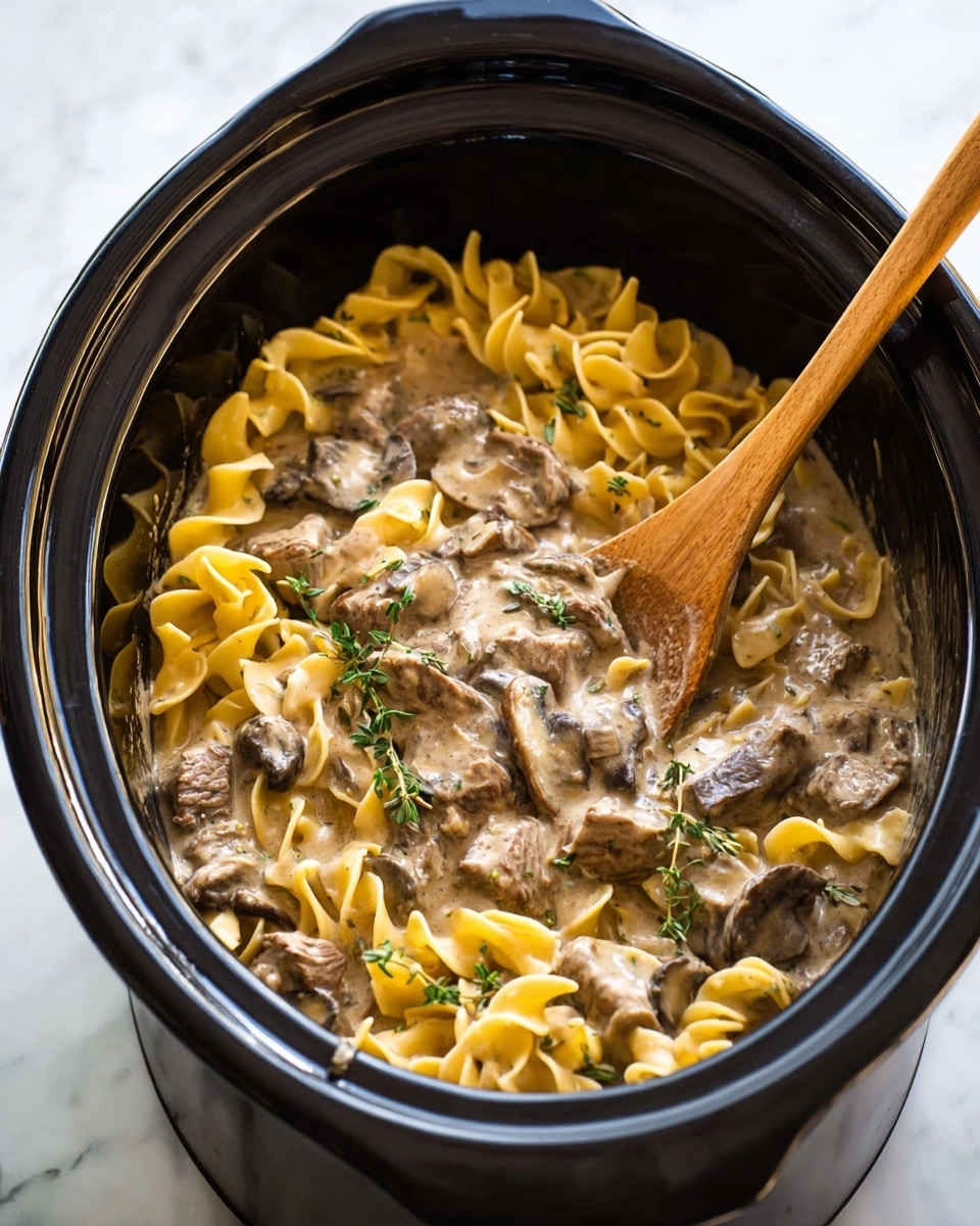 A white plate filled with soft, curly yellow egg noodles forms the base layer, topped with tender, browned strips of beef and thick slices of cooked mushrooms, all mixed and coated in a creamy, light brown sauce. Scattered finely chopped green herbs add a fresh pop of color on top. The dish rests on a white marbled surface with a blue-striped cloth partially underneath the plate, and silver forks are placed nearby. Small bowls with green herbs and salt can be seen blurred in the background. Photo taken with an iphone --ar 4:5 --v 7