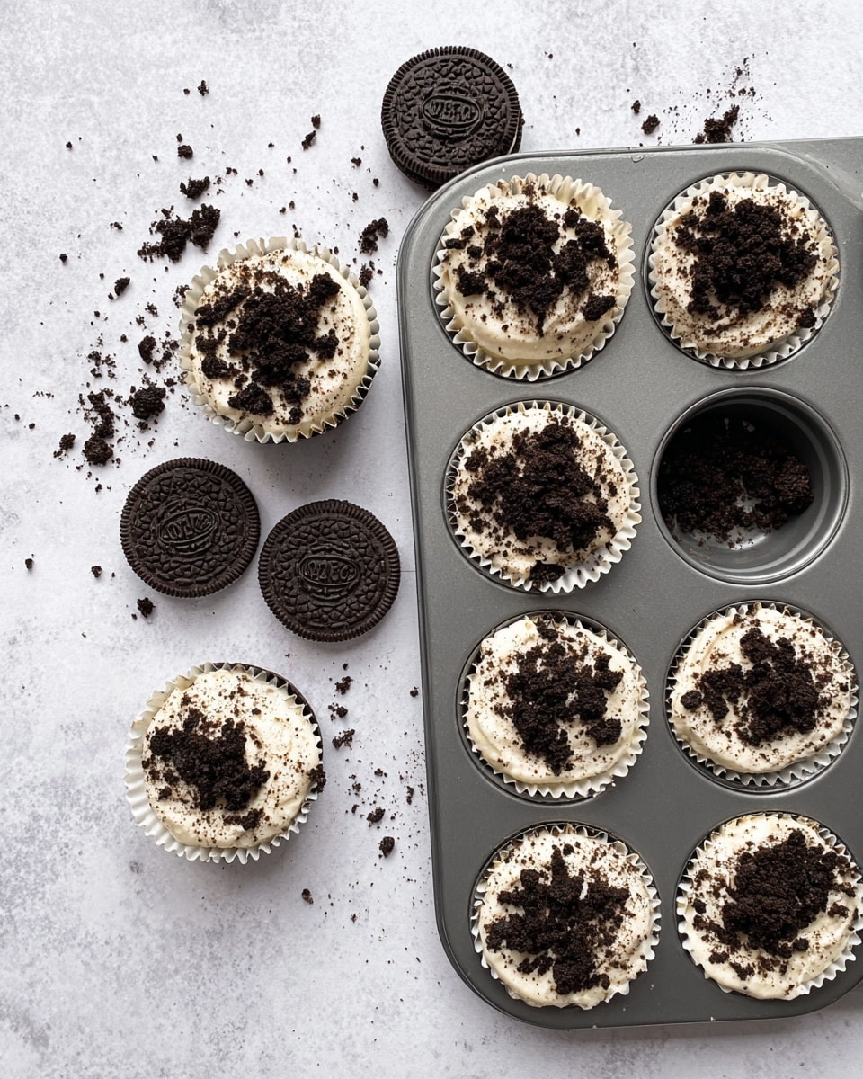 The image shows mini cheesecake bites arranged on a white plate and a white marbled surface. Each cheesecake bite has three layers: a dark chocolate cookie base, a thick middle layer of creamy, light beige cheesecake mixed with small dark cookie bits, and a crumbly dark chocolate cookie topping. One cheesecake bite in front has a small bite taken out, revealing all layers clearly. The background is softly blurred, focusing sharply on the front cheesecake bite. Photo taken with an iphone --ar 4:5 --v 7